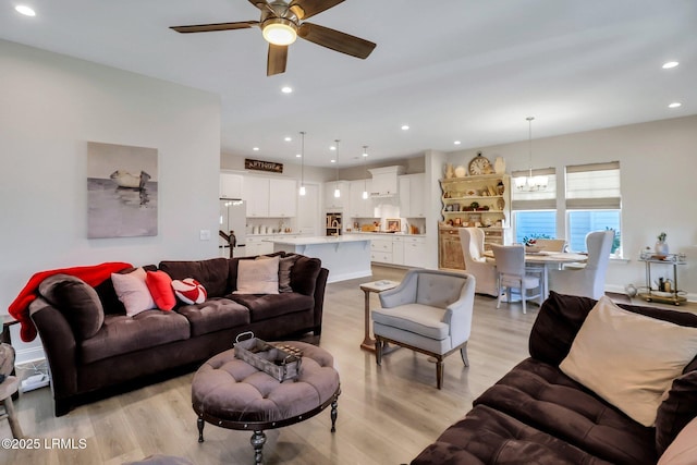 living room featuring ceiling fan with notable chandelier and light wood-type flooring