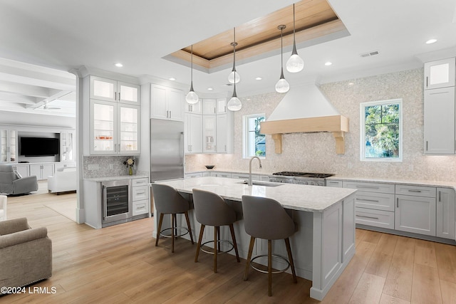 kitchen with pendant lighting, sink, a tray ceiling, custom exhaust hood, and beverage cooler