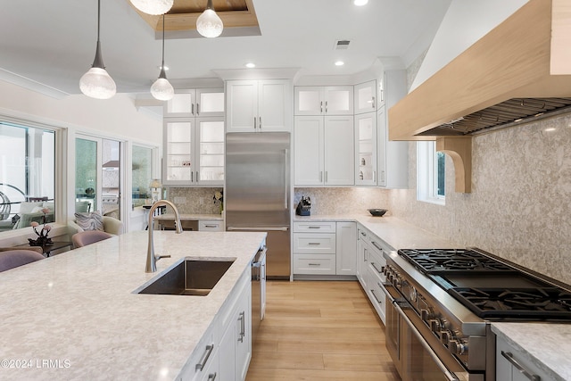 kitchen with premium range hood, pendant lighting, white cabinetry, sink, and high end appliances