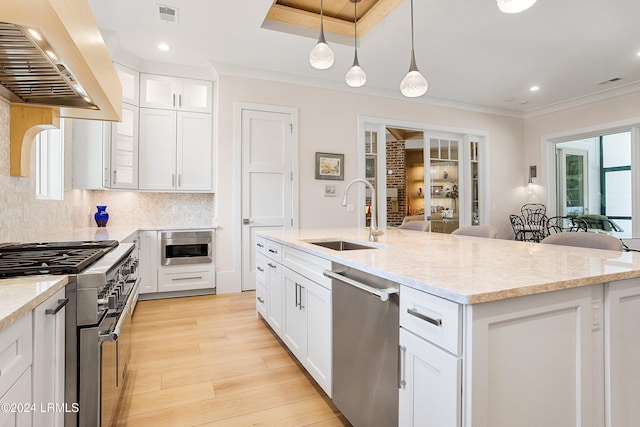 kitchen with sink, appliances with stainless steel finishes, custom range hood, pendant lighting, and white cabinets