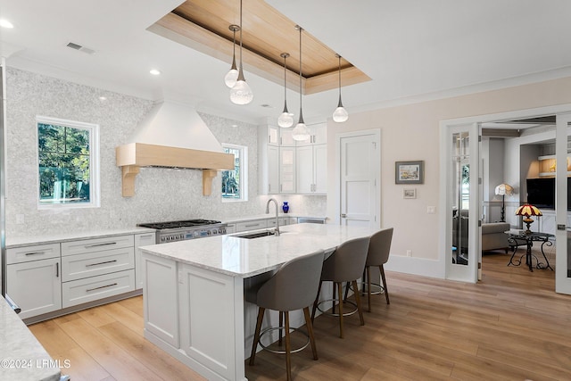 kitchen with hanging light fixtures, a raised ceiling, white cabinets, and premium range hood