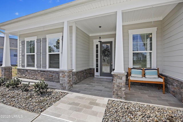 view of exterior entry featuring stone siding and covered porch