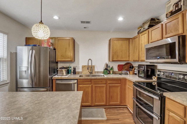 kitchen featuring appliances with stainless steel finishes, sink, hanging light fixtures, and light hardwood / wood-style flooring