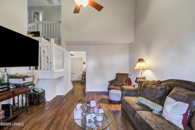 living room featuring dark wood-type flooring, ceiling fan, and a towering ceiling