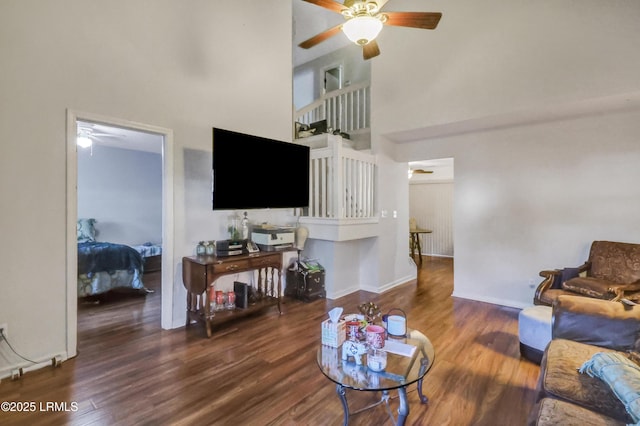 living room featuring dark wood-type flooring, ceiling fan, and a towering ceiling