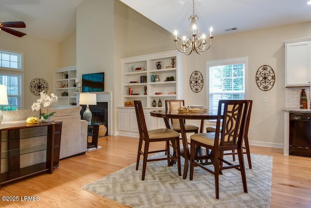 dining area with ceiling fan with notable chandelier, vaulted ceiling, and light hardwood / wood-style floors