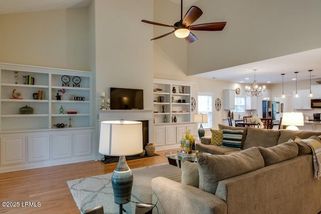 living room with ceiling fan with notable chandelier, high vaulted ceiling, and light hardwood / wood-style floors