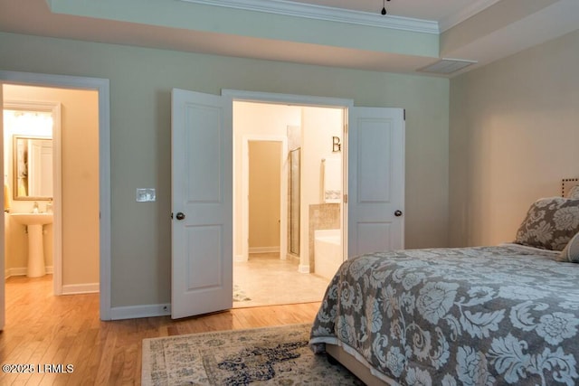 bedroom featuring ornamental molding, ensuite bathroom, and light hardwood / wood-style flooring