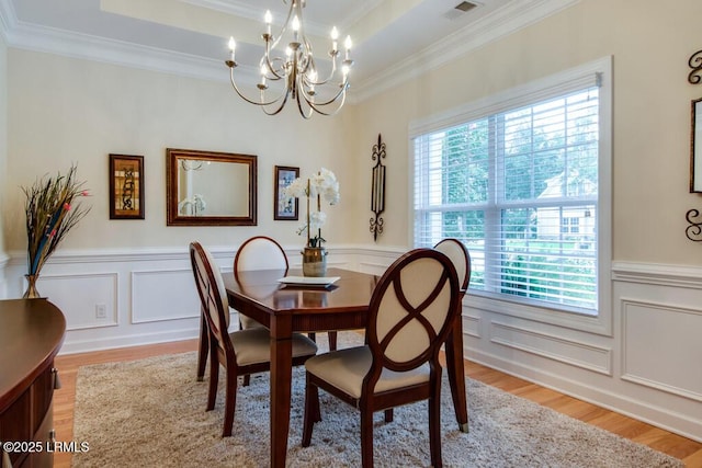 dining area with a tray ceiling, crown molding, light hardwood / wood-style flooring, and a chandelier