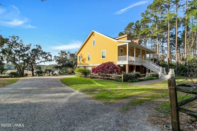 view of side of property featuring covered porch, stairs, gravel driveway, and a yard