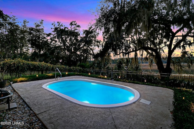 pool at dusk with a patio area and fence