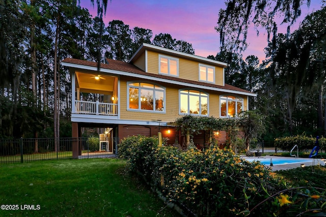 back of house at dusk with a balcony, a lawn, a fenced in pool, and fence private yard