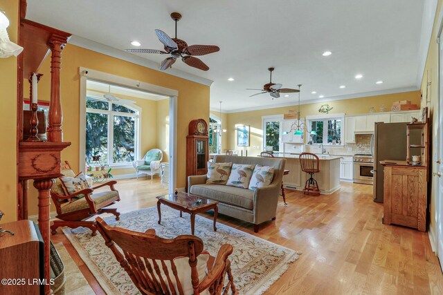 living room featuring crown molding, baseboards, light wood-type flooring, recessed lighting, and a ceiling fan