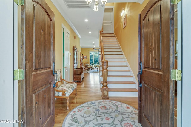 foyer with visible vents, ornamental molding, arched walkways, light wood finished floors, and stairs