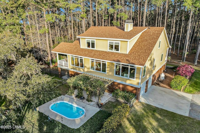 view of front of home with a fenced in pool, roof with shingles, a chimney, a yard, and driveway