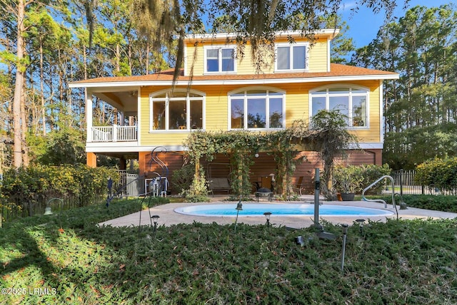 back of property with a balcony, fence, and an outdoor pool