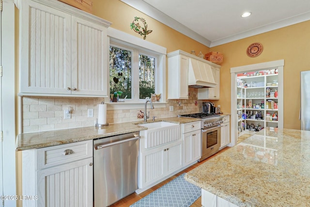 kitchen featuring custom range hood, a sink, light stone counters, backsplash, and stainless steel appliances