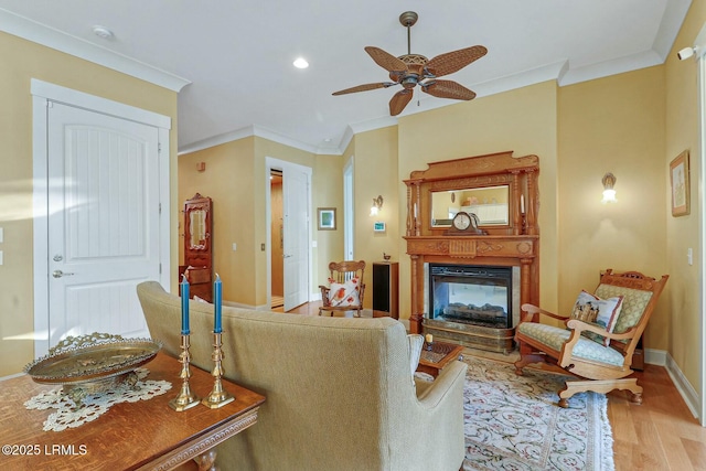 living room with wood finished floors, baseboards, a multi sided fireplace, ceiling fan, and crown molding