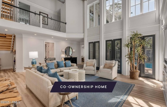 living room with french doors, a towering ceiling, ornamental molding, and light hardwood / wood-style floors