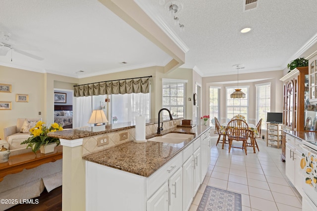 kitchen with a sink, dark stone counters, light tile patterned floors, a textured ceiling, and a kitchen island with sink