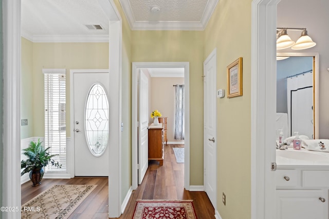 entryway with baseboards, visible vents, dark wood-type flooring, a textured ceiling, and crown molding