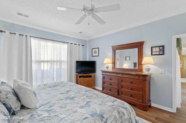 bedroom with wood finished floors, baseboards, visible vents, ornamental molding, and a textured ceiling