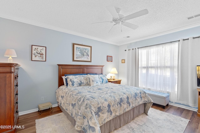 bedroom with visible vents, a textured ceiling, wood finished floors, and crown molding