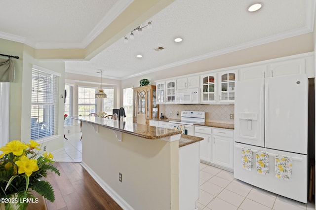 kitchen with white appliances, stone counters, a kitchen bar, crown molding, and tasteful backsplash