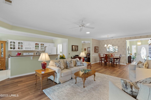 living area with visible vents, wallpapered walls, ornamental molding, ceiling fan with notable chandelier, and light wood-style floors
