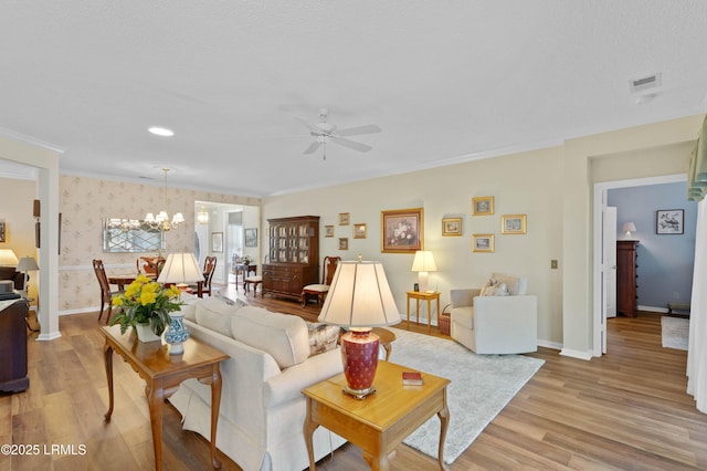 living area featuring baseboards, ceiling fan with notable chandelier, light wood-style flooring, and wallpapered walls