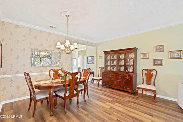 dining space featuring wood finished floors, baseboards, wallpapered walls, ornamental molding, and a notable chandelier