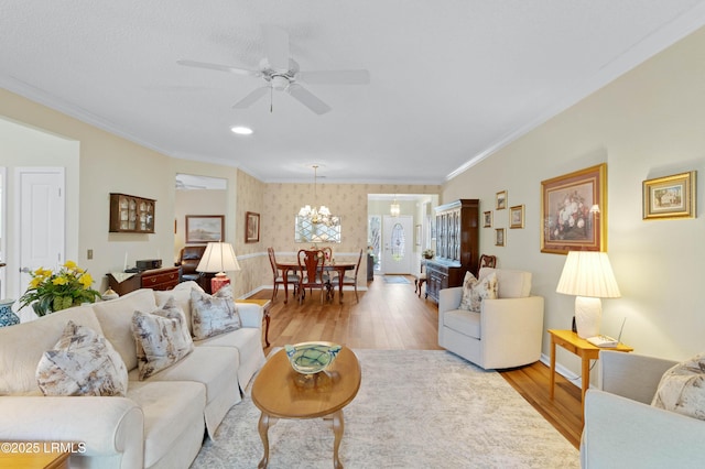 living room with ceiling fan with notable chandelier, light wood-style floors, crown molding, wallpapered walls, and baseboards