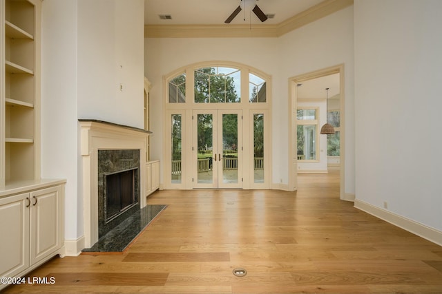 unfurnished living room featuring french doors, crown molding, light wood-type flooring, ceiling fan, and a premium fireplace