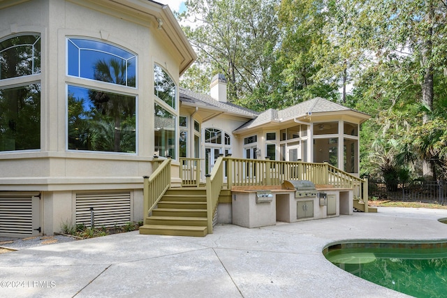 rear view of property featuring an outdoor kitchen, a swimming pool side deck, a sunroom, and a patio area