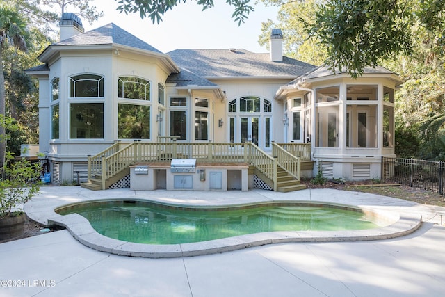 back of property featuring a fenced in pool, a patio area, a sunroom, and exterior kitchen