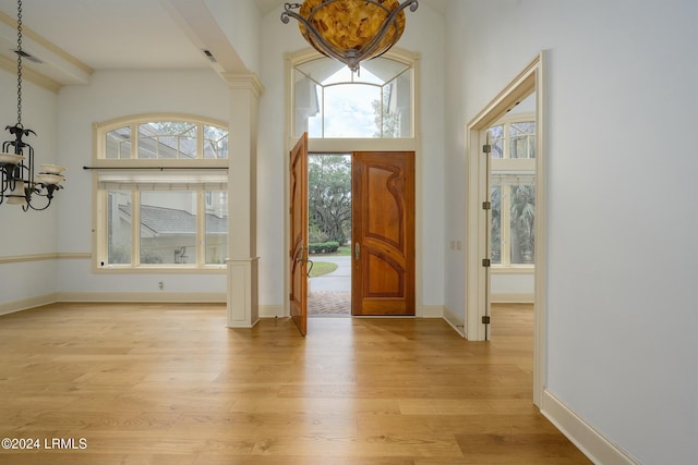 entryway with a notable chandelier, a towering ceiling, light hardwood / wood-style floors, and ornate columns