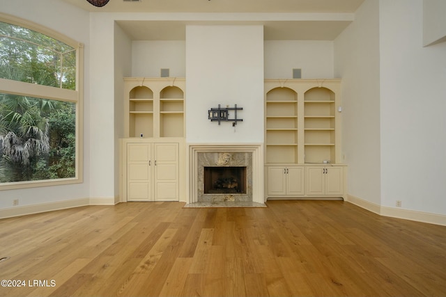 unfurnished living room with a premium fireplace, light hardwood / wood-style floors, built in features, and a high ceiling