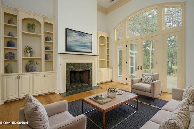 living room featuring ornamental molding, light wood-type flooring, a towering ceiling, french doors, and a premium fireplace
