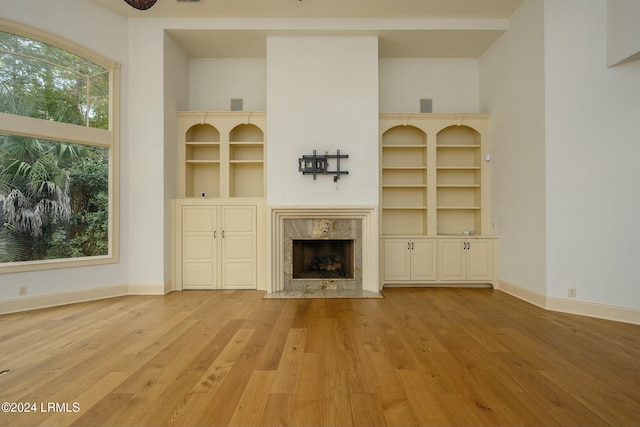 unfurnished living room featuring built in features, baseboards, wood finished floors, and a fireplace