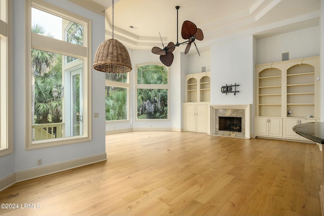 unfurnished living room with plenty of natural light, a tray ceiling, a fireplace, and built in shelves