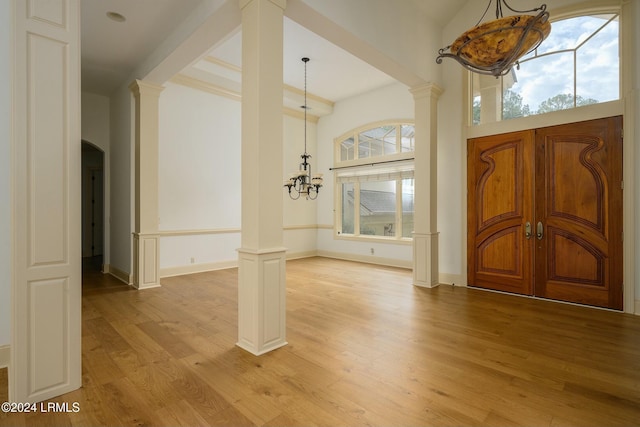 entryway with a notable chandelier, light wood-type flooring, and ornate columns