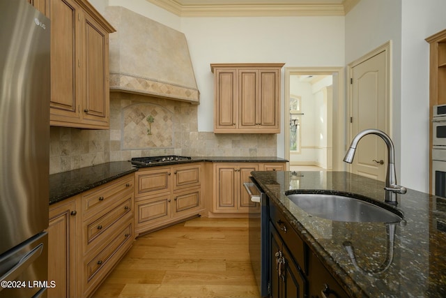 kitchen with premium range hood, sink, light hardwood / wood-style flooring, dark stone countertops, and stainless steel appliances