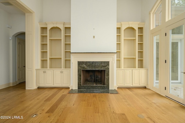 unfurnished living room featuring light wood-type flooring, a high end fireplace, and a towering ceiling