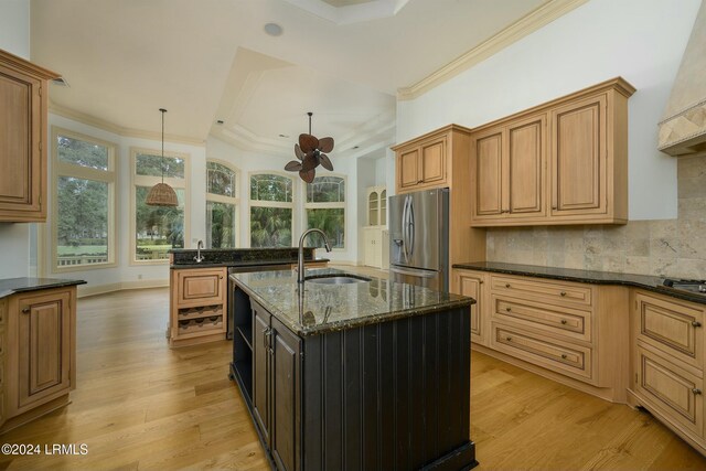 kitchen featuring an island with sink, sink, dark stone counters, stainless steel fridge with ice dispenser, and light wood-type flooring