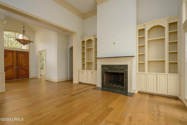 unfurnished living room with a towering ceiling, built in features, crown molding, a premium fireplace, and light hardwood / wood-style flooring