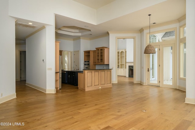 kitchen featuring sink, hanging light fixtures, a tray ceiling, crown molding, and light hardwood / wood-style flooring