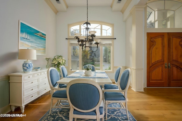 dining area featuring light wood-style floors, a decorative wall, wainscoting, and an inviting chandelier