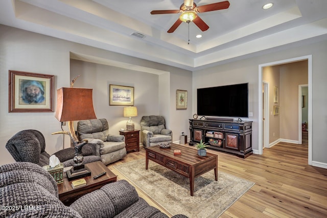 living room featuring a tray ceiling, light hardwood / wood-style flooring, and ceiling fan