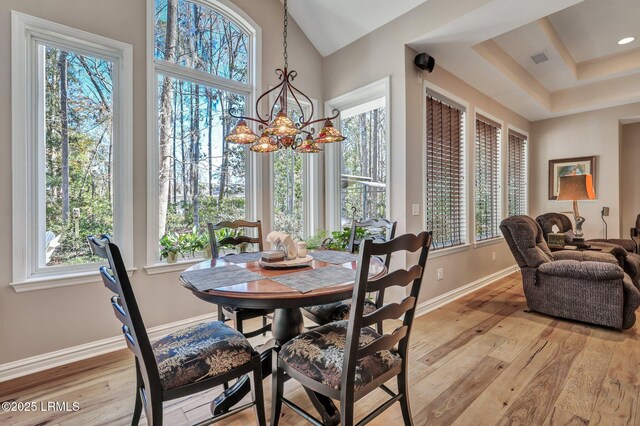 dining space featuring a towering ceiling, a tray ceiling, light hardwood / wood-style floors, and a notable chandelier