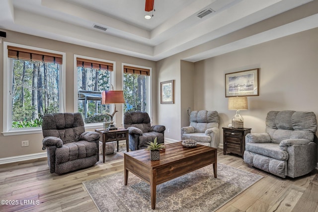 living room featuring light hardwood / wood-style flooring, ceiling fan, and a tray ceiling